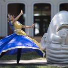 A dancer in blue and gold Indian attire twirls next to an egghead sculpture
